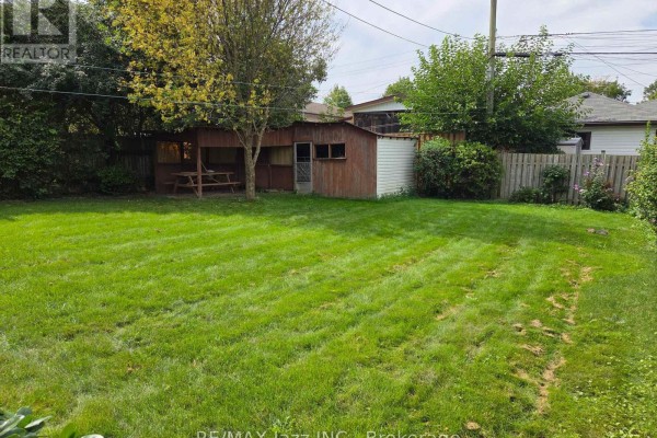 Backyard view with a wooden shed, covered picnic area, and a large, grassy lawn. - 302 Poplar Street, Oshawa