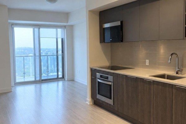 Open concept apartment kitchen with dark wood cabinets, stainless steel appliances, and light wood floors. - 3020 - 2031 Kennedy Road, Toronto