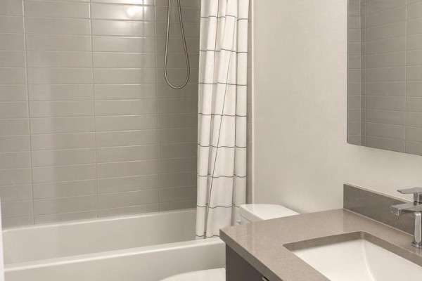 Apartment bathroom with a bathtub, gray tile shower surround, toilet, and vanity. - 3020 - 2031 Kennedy Road, Toronto
