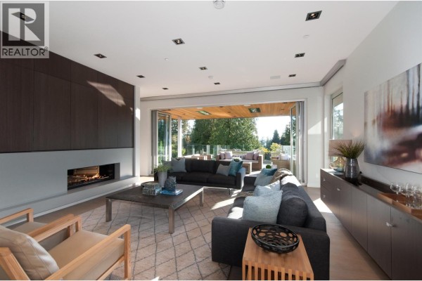 Living room with a long linear fireplace, dark grey sectional sofa, and folding glass doors opening to an outdoor patio. - 3023 Mathers Avenue, West Vancouver