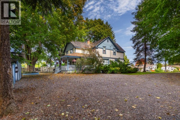 View of the white and blue house from a gravel driveway with fallen autumn leaves. - 3025 Patterson Street, Armstrong