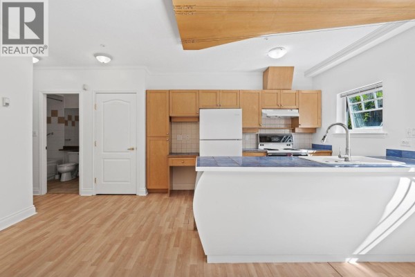 Kitchen with light wood cabinets, white appliances, and a doorway to a bathroom. - 3027 W 7th Avenue, Vancouver