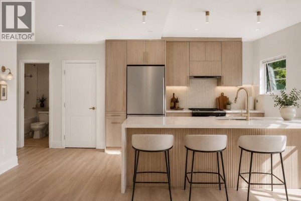 Renovated kitchen with wood cabinets, stainless steel fridge, and breakfast bar. - 3027 W 7th Avenue, Vancouver