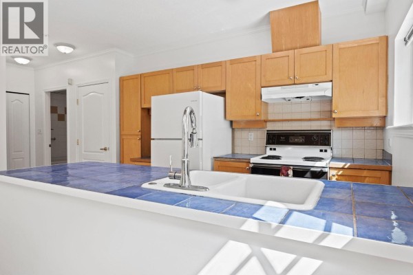 Kitchen with blue tile counters, wood cabinets, white appliances, and a large sink. - 3027 W 7th Avenue, Vancouver