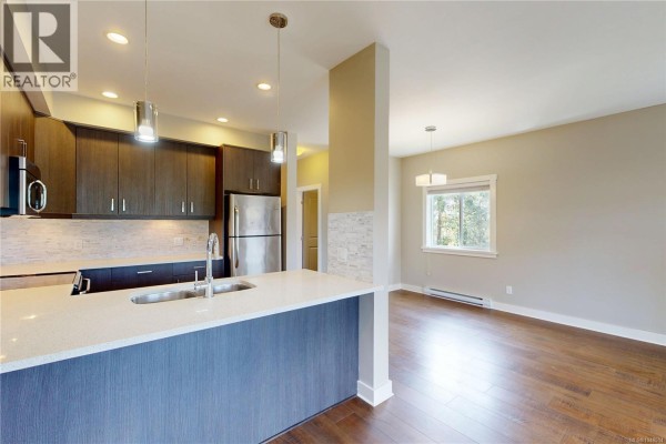 Open-concept kitchen and dining area with dark wood cabinets, stainless steel refrigerator, and hardwood floors. - 3028 Urban Creek Way, Langford