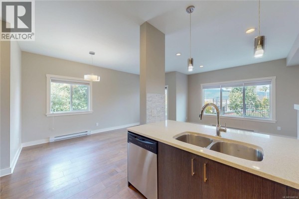 Kitchen island with double sink overlooking an open living space with large windows and mountain views. - 3028 Urban Creek Way, Langford