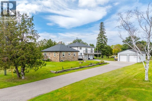 View of a stone house and a white house with a balcony, set back from a paved driveway with a metal garage. - 3029 Burnhamthorpe Road W, Milton