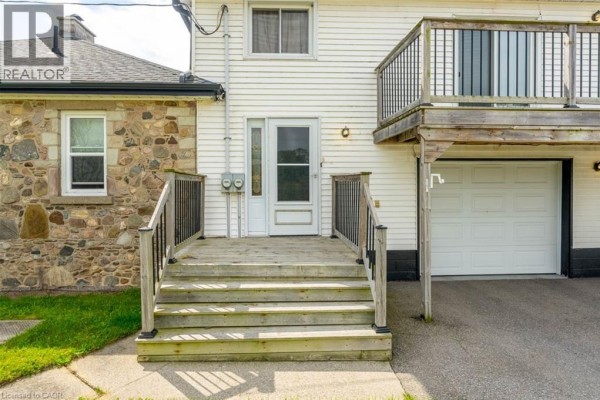 Close-up of a wooden deck leading to a white door between a stone wall and a garage door. - 3029 Burnhamthorpe Road W, Milton
