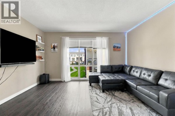 Living room with a large black sectional sofa, dark grey floor, and a window view. - 303, 125 Caribou Crescent, Red Deer