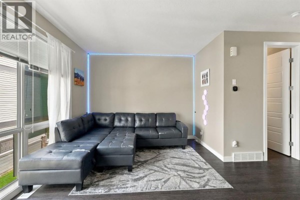 Living room showing a black sectional sofa, grey rug, and a doorway leading to another room. - 303, 125 Caribou Crescent, Red Deer