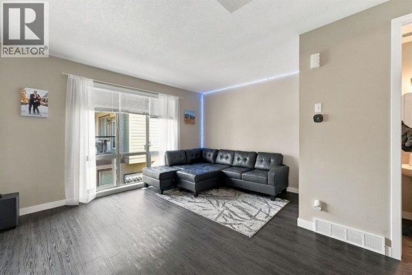 Living room with a sectional sofa, view down a hallway, and stairs leading upstairs. - 303, 125 Caribou Crescent, Red Deer