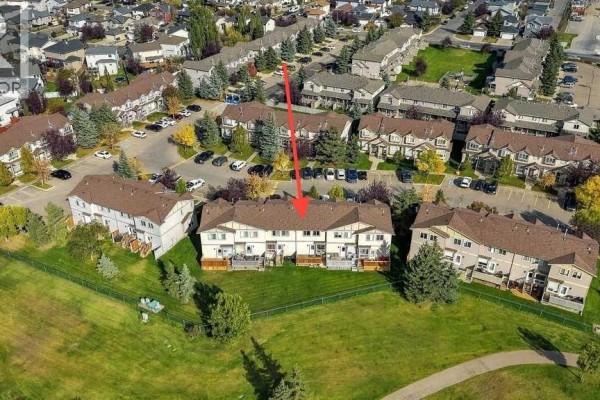 Aerial view of a townhouse complex with a red arrow pointing to the specific unit at 303, 2005 Luxstone Boulevard Sw. - 303, 2005 Luxstone Boulevard Sw, Airdrie