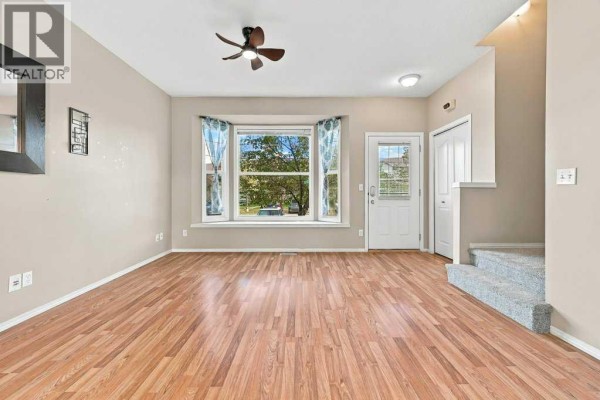 Entryway of a townhouse with wood laminate flooring, a closet, a carpeted staircase, and a window with patterned curtains. - 303, 2005 Luxstone Boulevard Sw, Airdrie