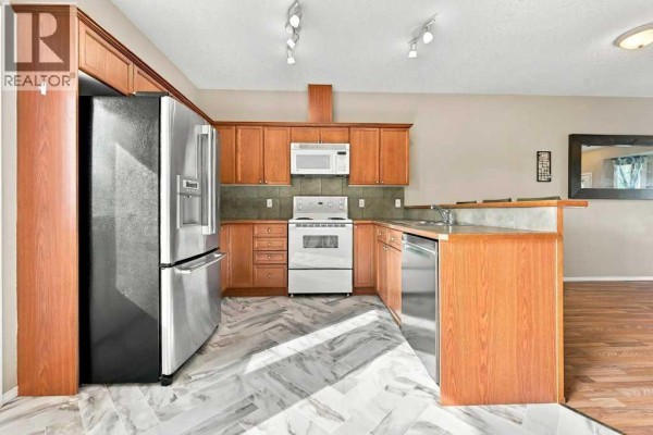Living room with light wood laminate flooring, neutral walls, and a view of the kitchen island with bar stools. - 303, 2005 Luxstone Boulevard Sw, Airdrie