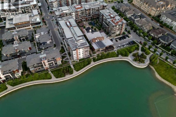 Aerial view of a multi-story apartment complex with a water feature and surrounding residential buildings. - 303, 2231 Mahogany Boulevard Se, Calgary