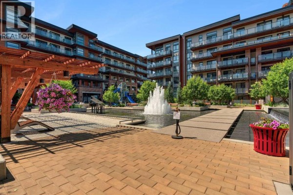 Courtyard of an apartment building featuring a fountain, seating area, and playground with brick paving. - 303, 2231 Mahogany Boulevard Se, Calgary