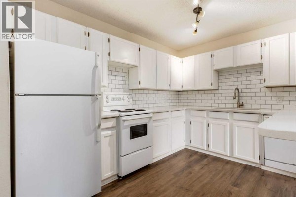 White kitchen with subway tile backsplash, white appliances, and dark wood-look flooring. - 303, 730 2 Avenue Nw, Calgary