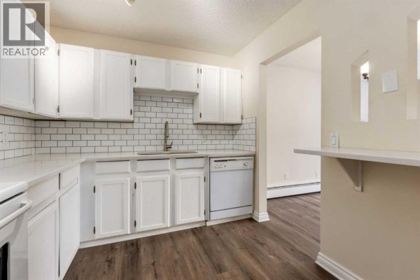 Kitchen view showing white cabinets, subway tile, sink, dishwasher, and pass-through. - 303, 730 2 Avenue Nw, Calgary