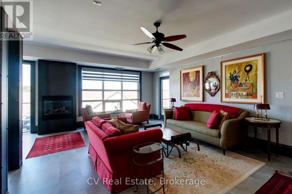 Living room with a fireplace, two sofas, armchairs, artwork, and a ceiling fan. - 303 - 1 Shipyard Lane, Collingwood