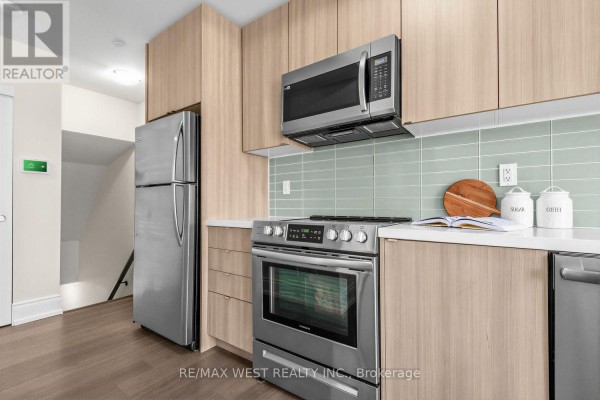 Kitchen with stainless steel appliances, light wood cabinets, and mint green backsplash. - 303 - 1150 Briar Hill Avenue, Toronto