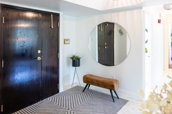 Foyer with dark wood double doors, a round mirror, and a brown bench. - 303 - 1700 The Collegeway, Mississauga