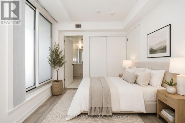 Bedroom with a queen-sized bed, light wood flooring, and a doorway to the bathroom. - 303 - 195 Commerce Street, Vaughan