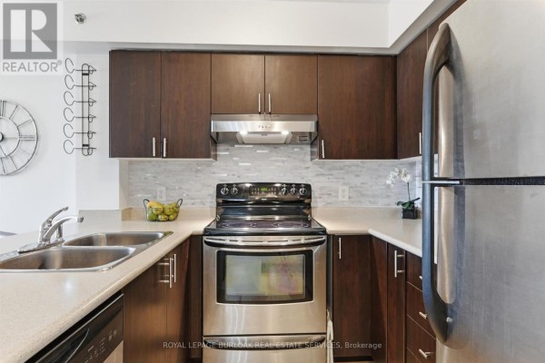 Kitchen with dark wood cabinets, stainless steel appliances, and a beige countertop and backsplash. - 303 - 3060 Rotary Way, Burlington