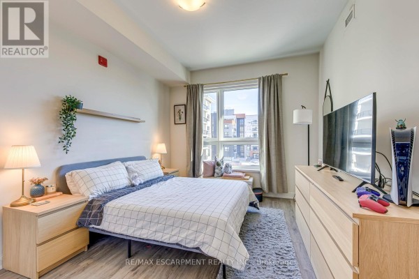 Bedroom with bed, nightstands, dresser, TV, gaming console, and city view window - 303 - 320 Plains Road E Burlington