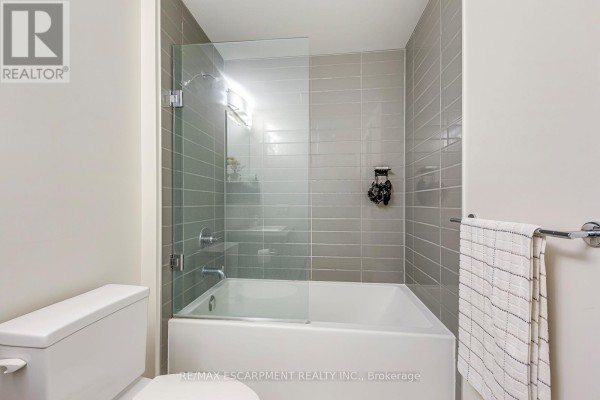Bathroom with bathtub, glass shower door, and tiled walls - 303 - 320 Plains Road E Burlington