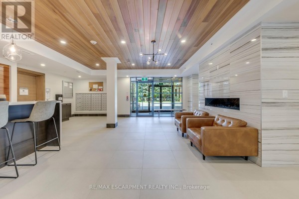 Building hallway with tiled floors, elevators, artwork, and a large window. - 303 - 320 Plains Road E, Burlington