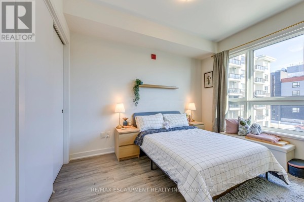Bedroom with grid bedding, window seat, and city view - 303 - 320 Plains Road E Burlington