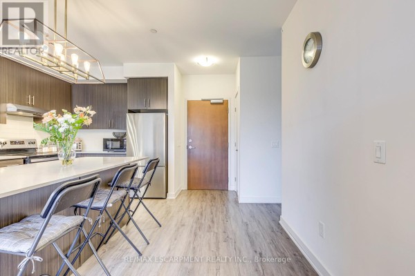 Modern kitchen with island, seating, stainless steel appliances, and wood-look floors - 303 - 320 Plains Road E Burlington