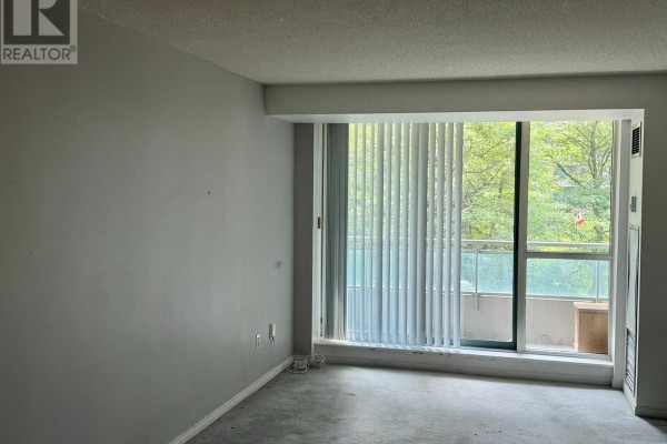 Interior view of an empty room with large windows, vertical blinds, and a balcony. - 303 - 39 Pemberton Avenue, Toronto