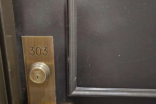 Close-up of a dark apartment door with a brass number plate reading "303" and a lock. - 303 - 480 Mclevin Avenue, Toronto