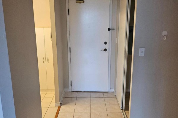 Apartment entryway with a white door, beige tiled floor, and white storage cabinets. - 303 - 480 Mclevin Avenue, Toronto