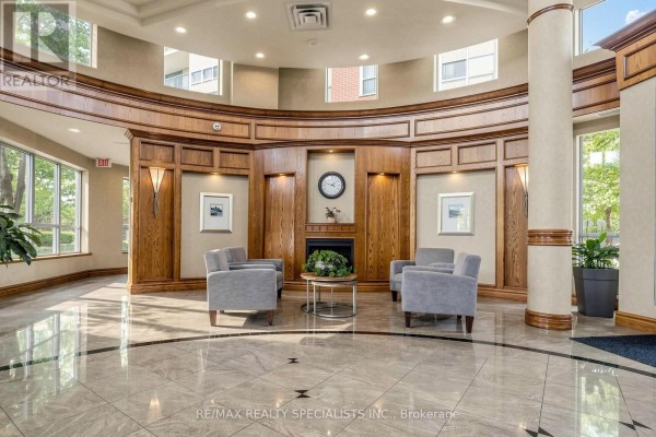 Lobby seating area with grey armchairs, a decorative fireplace, and wood accents. - 303 - 4879 Kimbermount Avenue, Mississauga