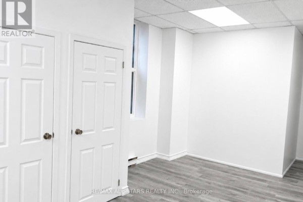 View of an empty room with light wood-look flooring, white walls, a window, and a light fixture. - 303 - 66 Gerrard Street E, Toronto