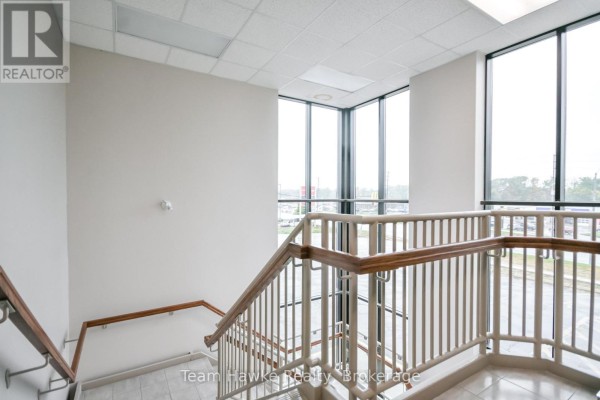 Upper level of an interior staircase with white walls, large corner windows, and railing. - 303 - 9170 County 93 Road, Midland