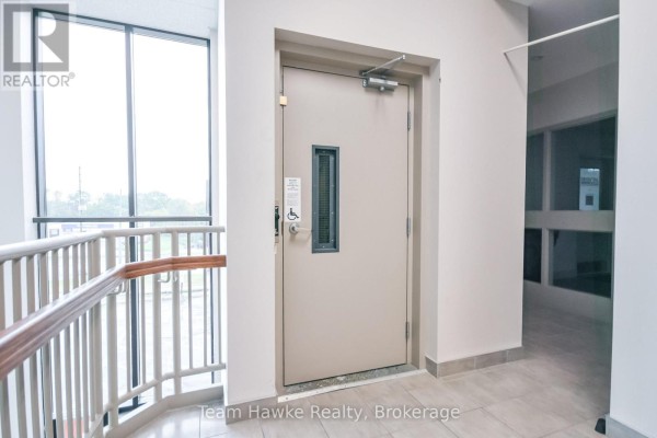 Light beige elevator door with a small window and accessibility symbol next to a hallway. - 303 - 9170 County 93 Road, Midland