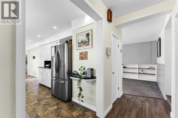 Kitchen area with stainless steel refrigerator, dark wood floors, and adjacent living room. - 303 10 Street Sw, Medicine Hat