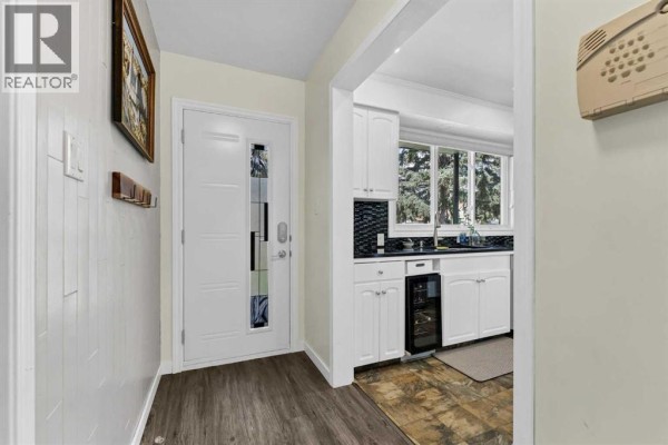 Interior view of the entrance hall with a white door, wood paneling, and a glimpse of the kitchen. - 303 10 Street Sw, Medicine Hat