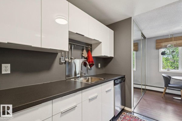 Narrow kitchen featuring white cabinets, dark countertops, and a stainless steel refrigerator. - #303 10838 108 St Nw, Edmonton