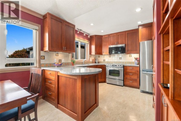 A compact kitchen with warm wood cabinets, granite countertops, and stainless steel appliances. - 303 1158 Fairfield Rd, Victoria