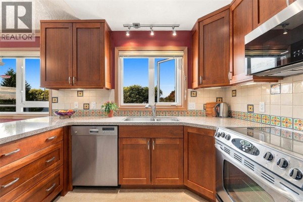Close-up of a kitchen sink area with wood cabinets, tiled backsplash, and garden view window. - 303 1158 Fairfield Rd, Victoria