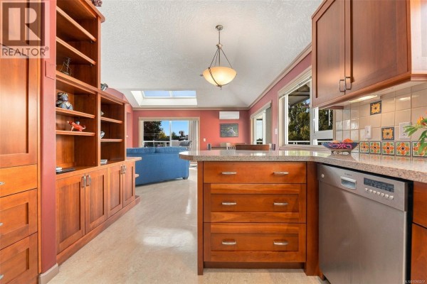 View from the kitchen into a living area with skylights, a blue sofa, and large windows. - 303 1158 Fairfield Rd, Victoria