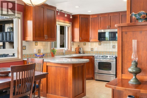 Kitchen corner showing wooden cabinetry, stainless steel appliances, and a window with a garden view. - 303 1158 Fairfield Rd, Victoria