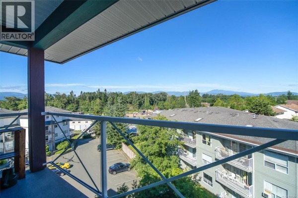 View from balcony overlooking a residential area with trees and mountains in the distance. - 303 129 Back Rd, Courtenay