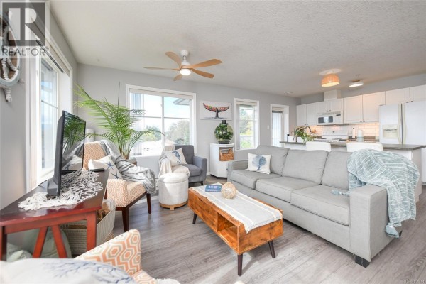 Living room and kitchen with gray sofa, island with bar stools, and light gray walls. - 303 129 Back Rd, Courtenay