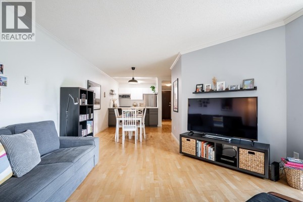 Living room with grey sofa, media unit, bookshelf, and view into the dining area and kitchen. - 303 1510 W 1st Avenue, Vancouver