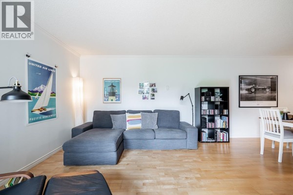 Living room featuring a grey L-shaped sofa, bookshelf, and artwork above a dining table. - 303 1510 W 1st Avenue, Vancouver
